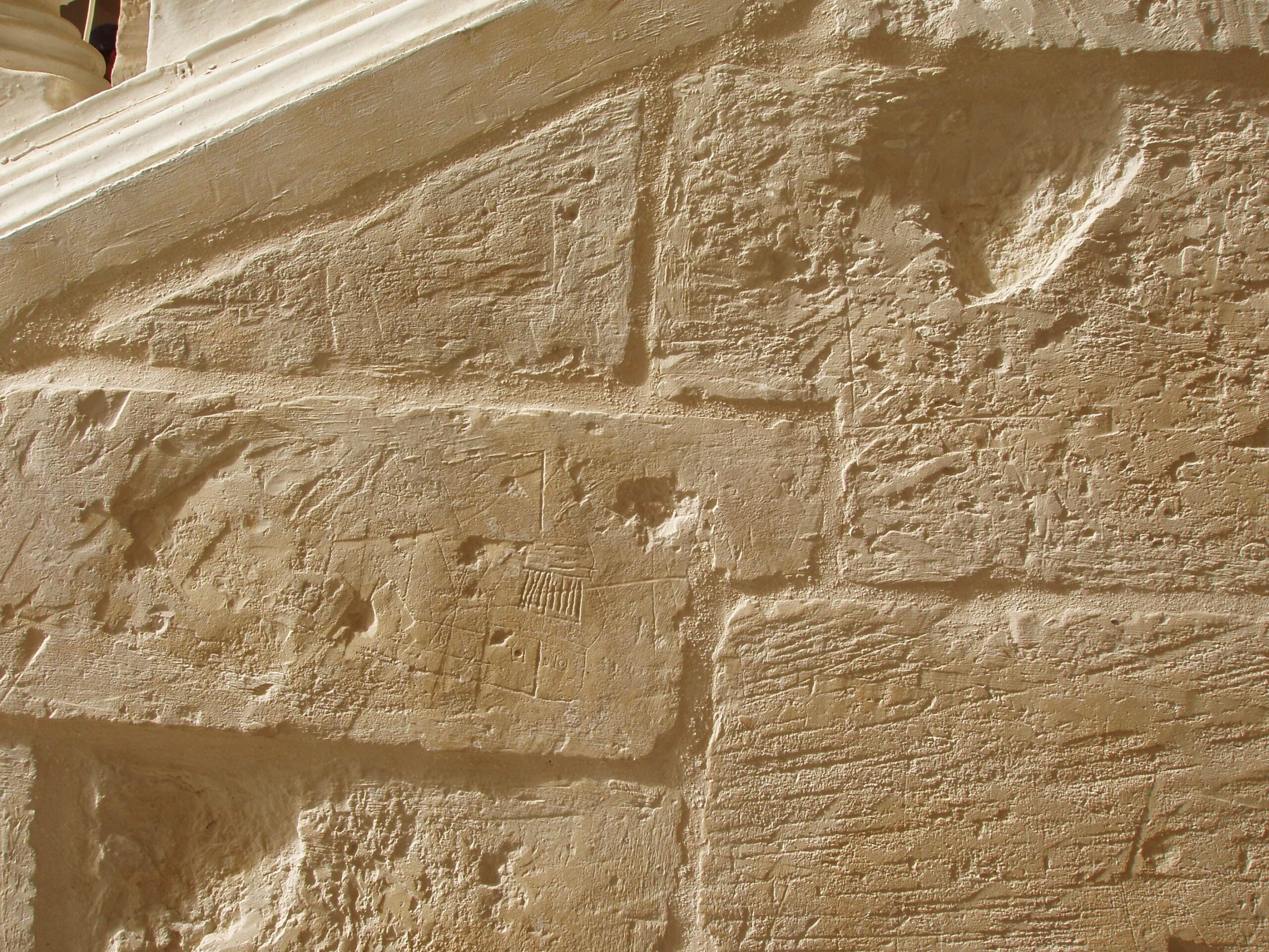 This example of a ship graffito is partially hidden due to works carried out on the stone. The decorated stern is visible together with a flag and two cannon ports.