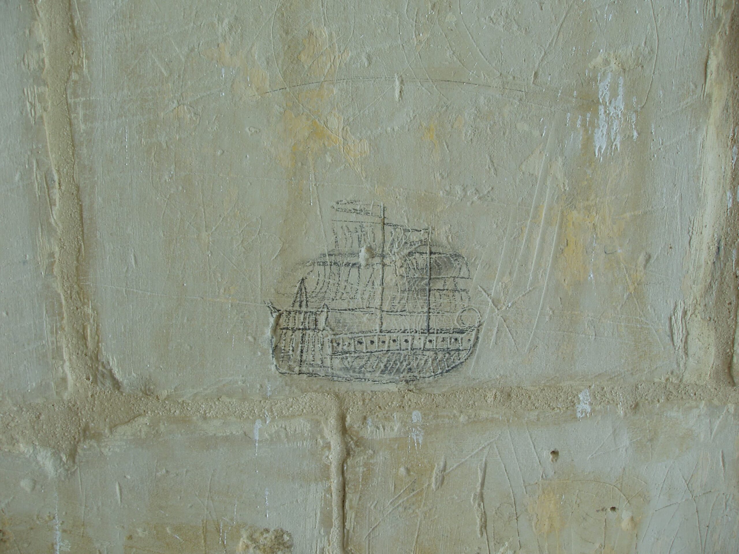 Drawn with a dark-coloured implement on the wall is a representation of a ship. The two masts carrying square rigging can be identified together with a tall stern and a row of cannon ports. Flags are depicted, flying from masts.