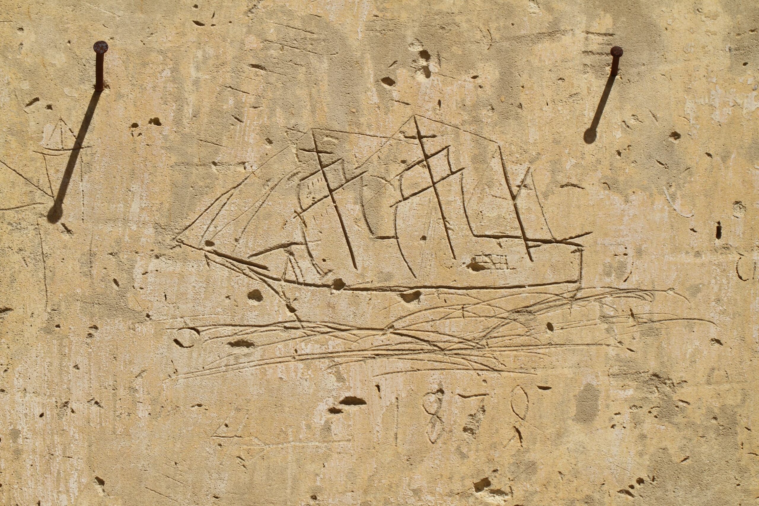 A three-dimensional depiction of a square rigged ship. The ship appears as heaving to portside. The numbers ‘1879’ etched under the graffito are probably related to the ship graffito.